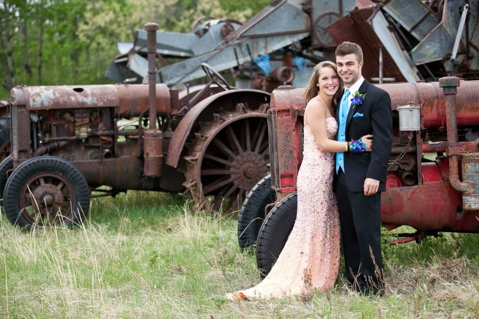 Prom Photographer a female and a male graduate pose together in front of rusted farm machinery