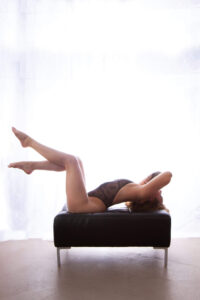 Saskatoon boudoir a woman in lingerie arches her back with her legs in the air in front of a bright white curtain